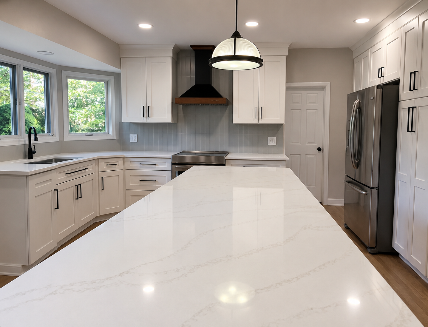 Modern kitchen with white cabinetry, marble countertop island, stainless steel appliances, black faucet, and large windows showing greenery outside.