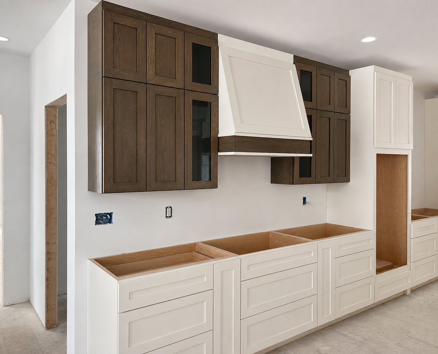 Kitchen cabinets under construction with white lower cabinets and dark upper cabinets, a white range hood, and open spaces for appliances or drawers.