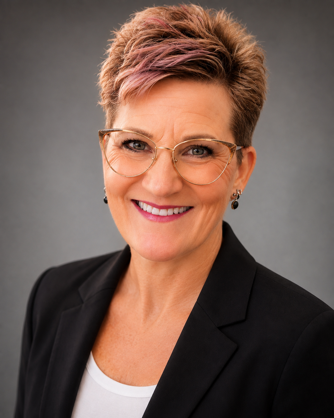 A professional woman with short, styled hair, wearing glasses, earrings, a black blazer, and a white top, smiling in front of a gray background.