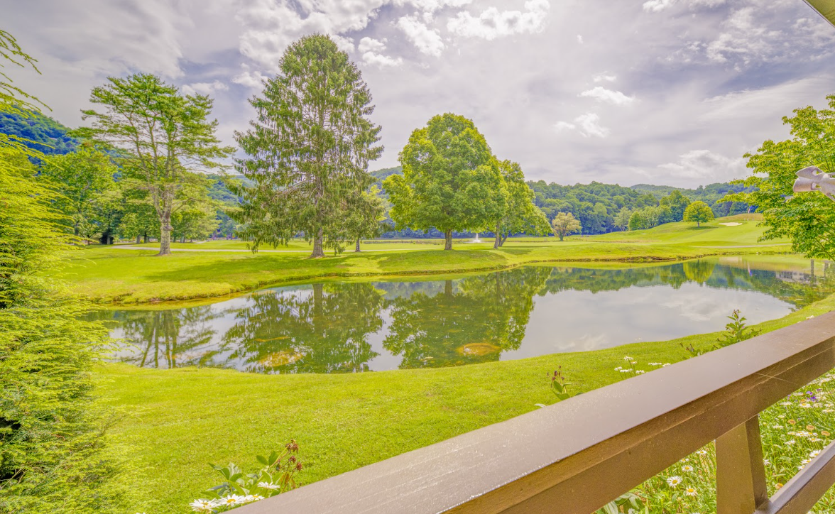 View of a serene golf course with a pond reflecting trees and a cloudy sky, taken from a wooden deck.