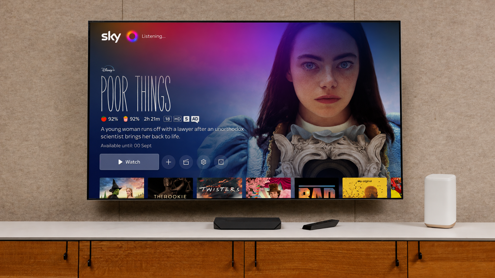 Living room TV displaying an entertainment interface with movie recommendations, alongside a voice remote and smart speaker.