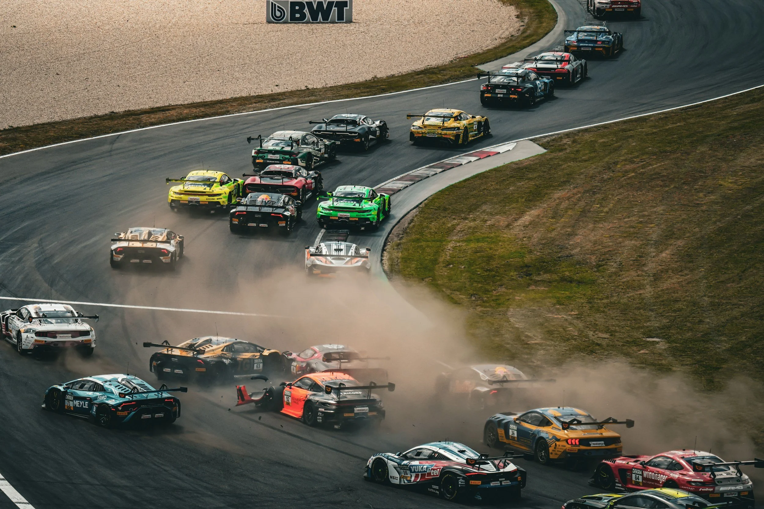 Multiple race cars are involved in a crash on a racetrack, with dust and debris in the air, some cars spinning out of control.