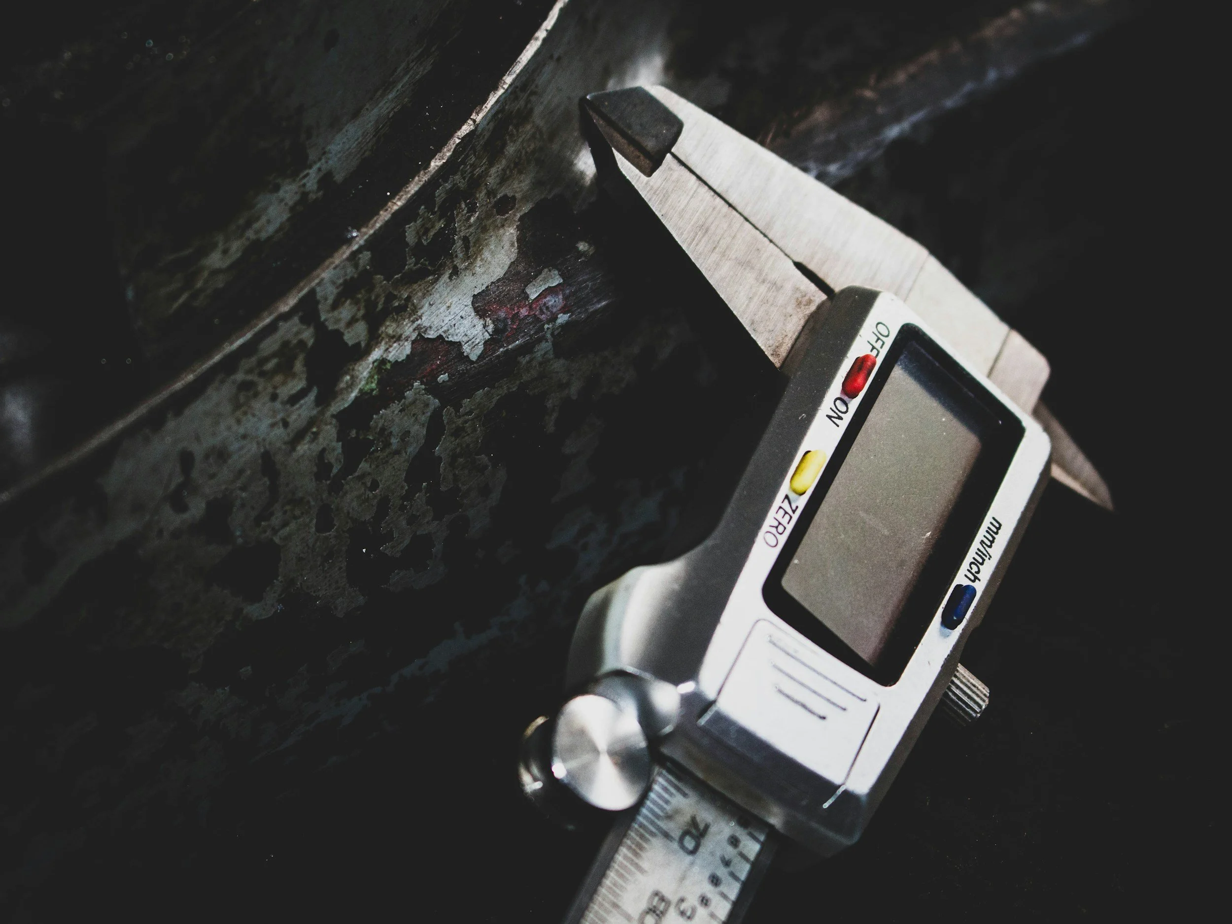 Digital caliper measuring a rusty metal surface in a close-up shot.