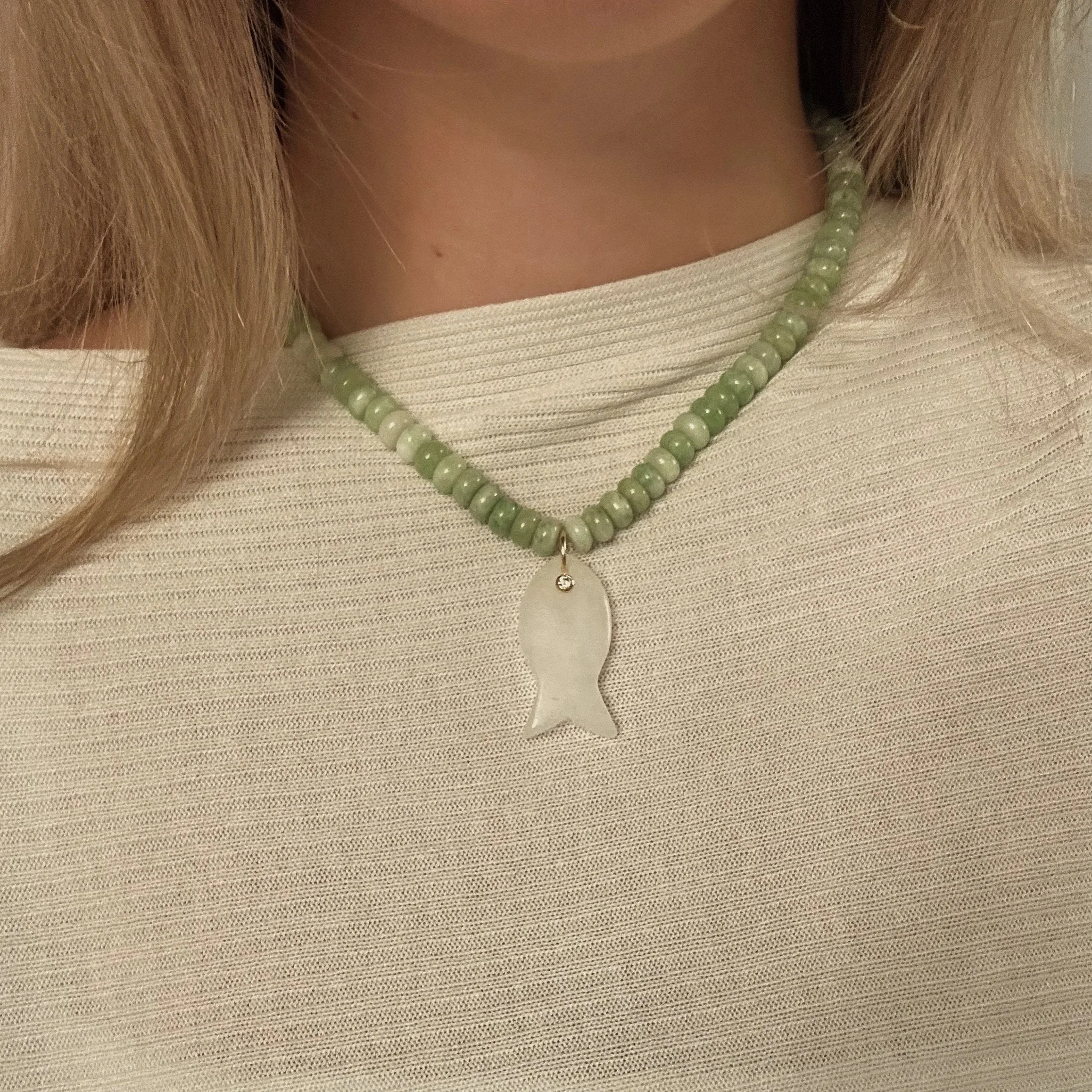 Close-up of a person wearing a beige top and a green beaded necklace with a pendant, and long blonde hair.