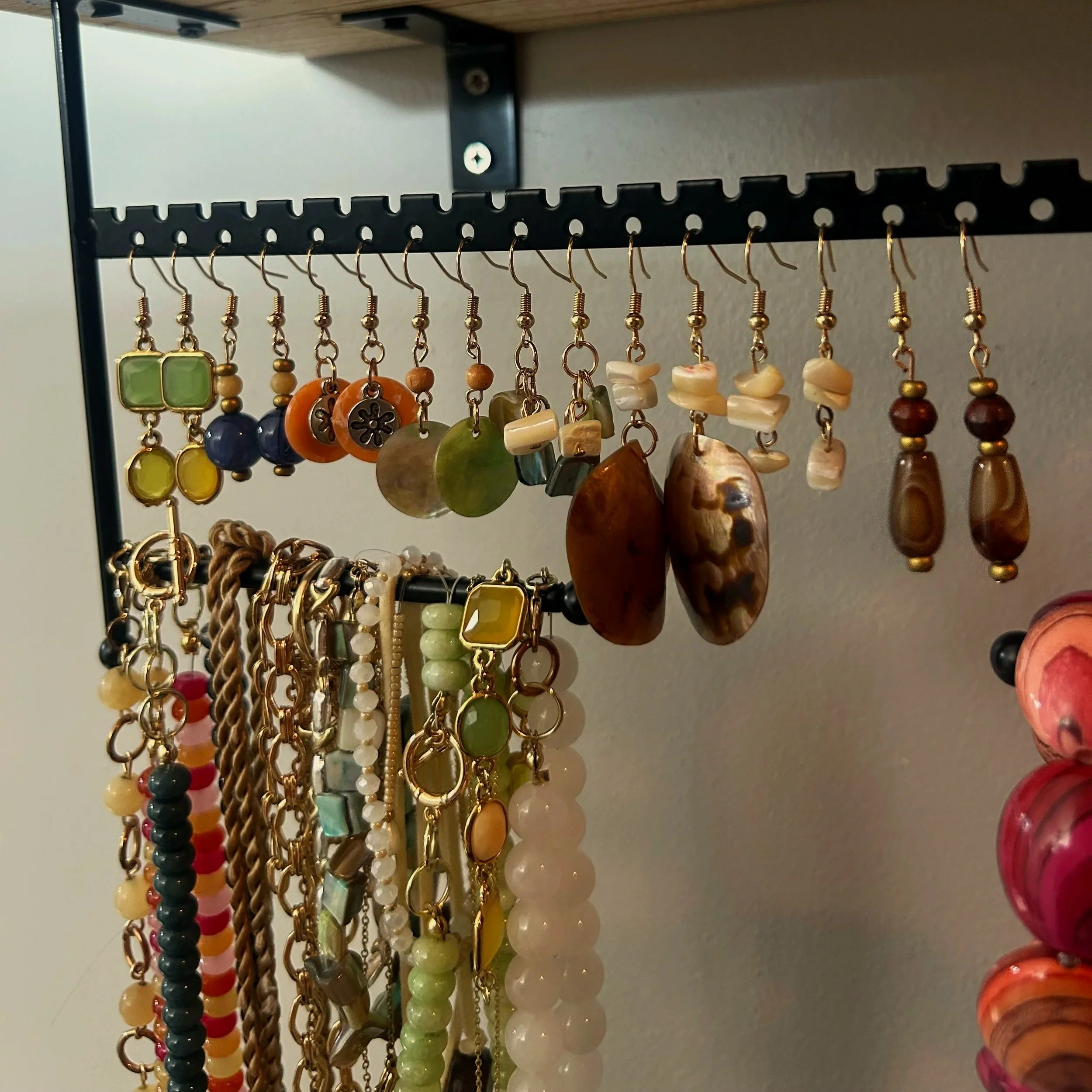 Close-up of a jewelry display with various beaded earrings hanging from a black rack mounted on a wooden shelf.