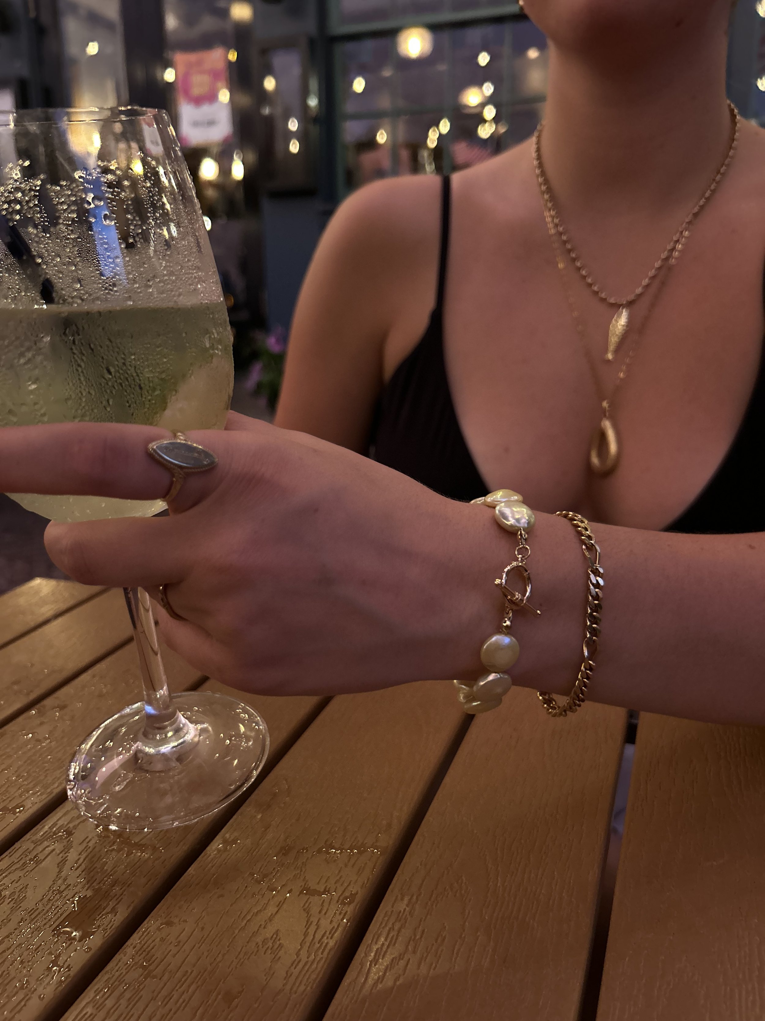 A woman wearing jewelry holding a glass of sparkling wine in a dimly lit indoor setting.