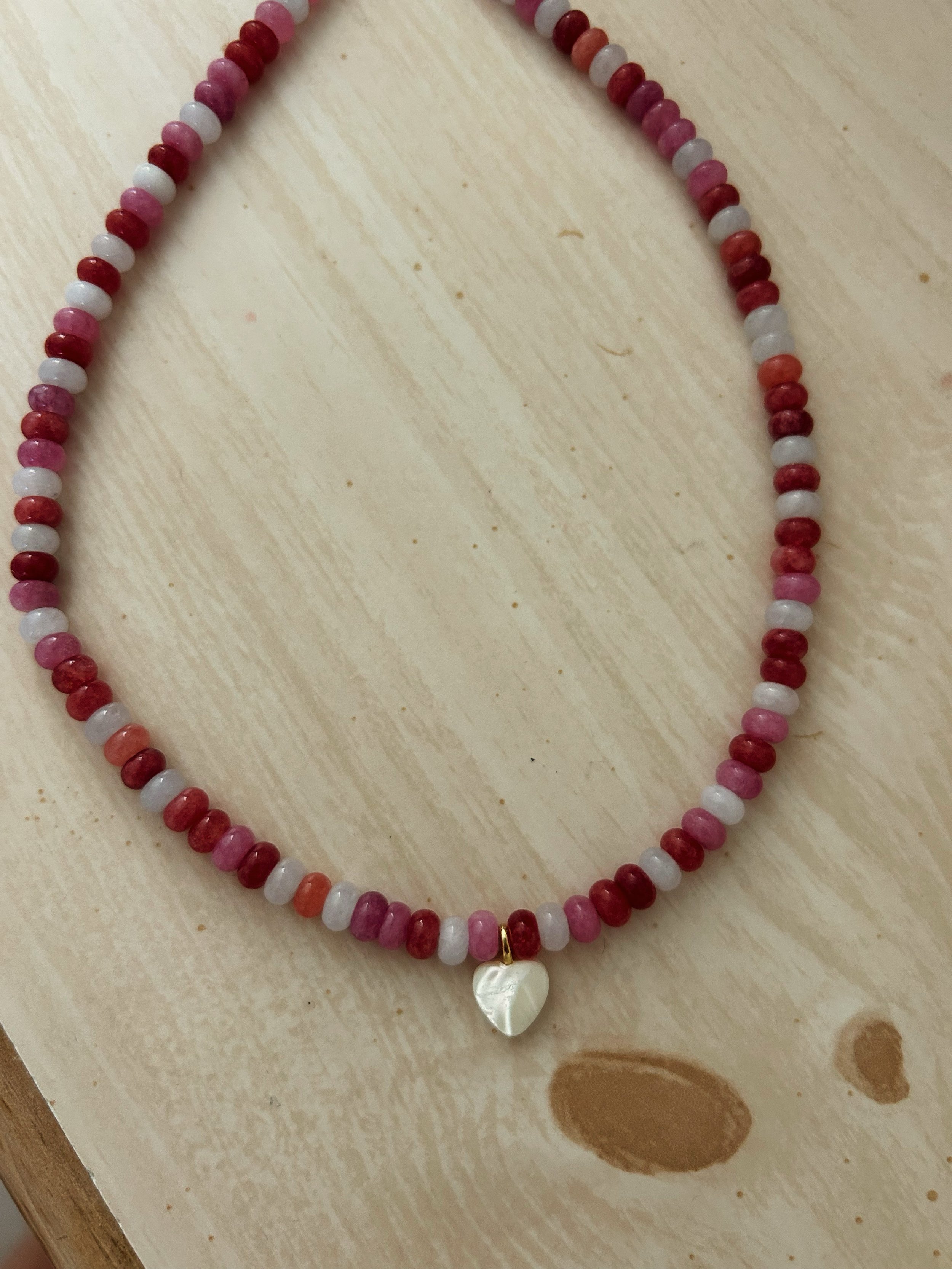 A beaded necklace with pink, red, and white beads and a heart-shaped pearl pendant.