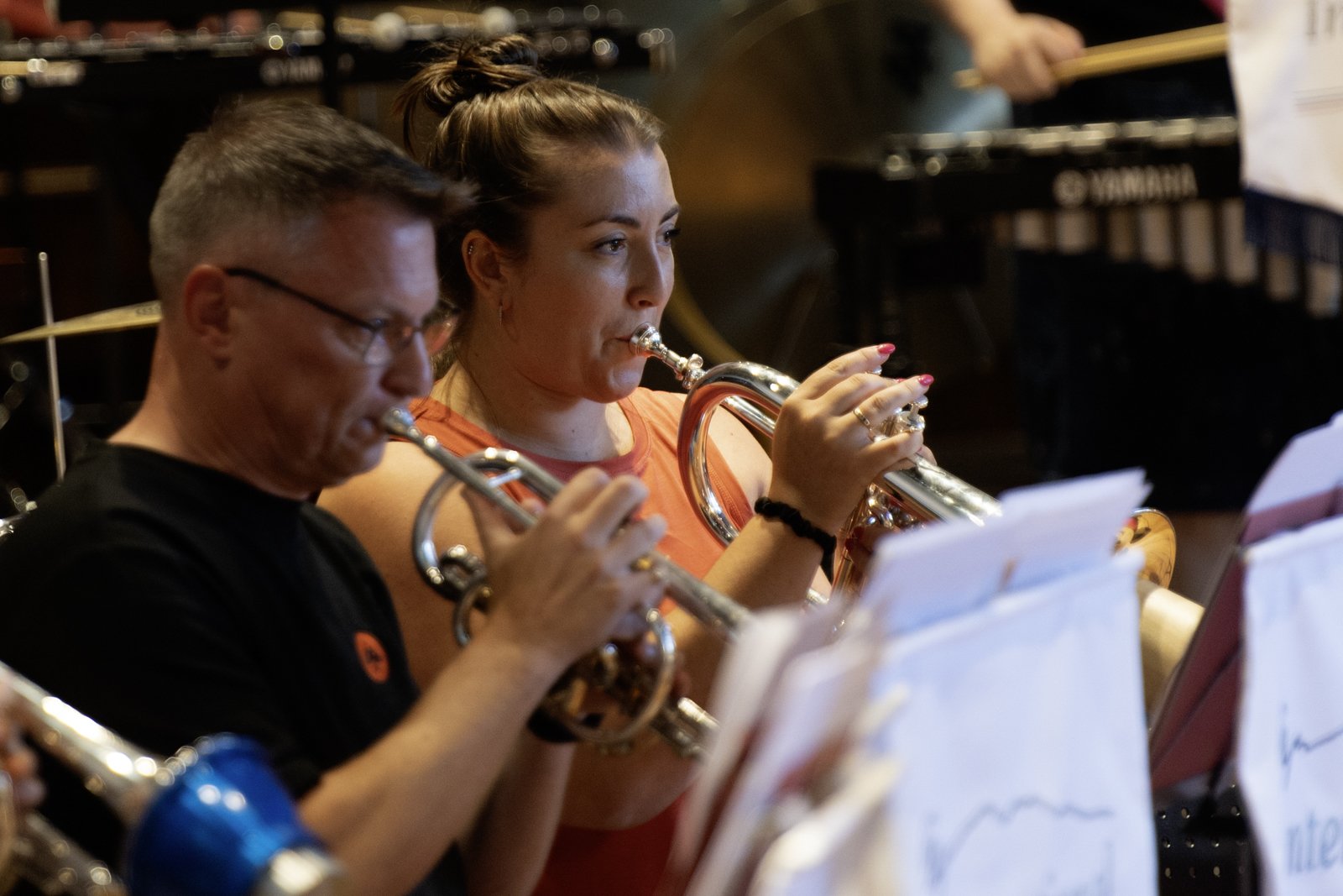 Two musicians, a man and a woman, playing flutes during a live performance with music sheets in front of them, in a setting that appears to be a concert or rehearsal space.