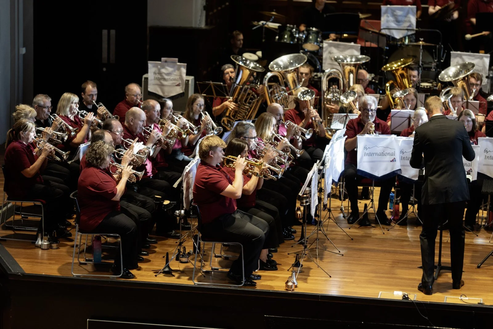 An orchestra performing on stage with musicians playing brass and percussion instruments, directed by a conductor.