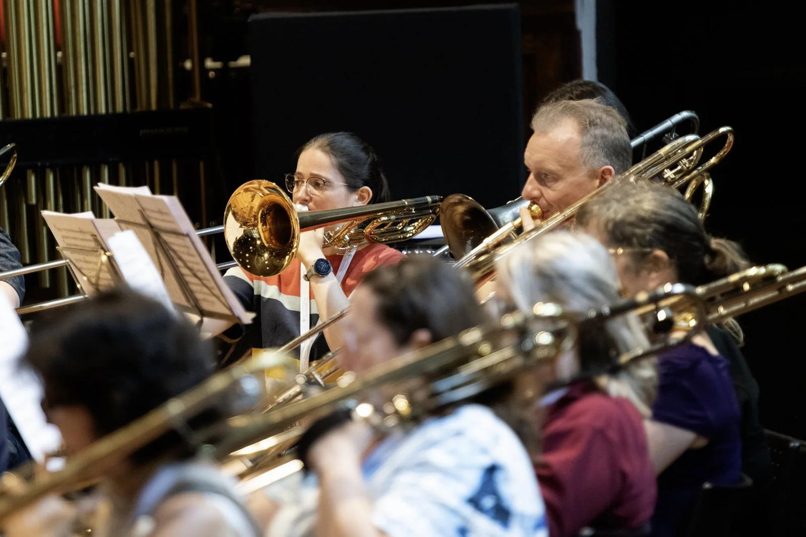 Orchestra musicians playing brass instruments, including trombones, during a rehearsal or concert.