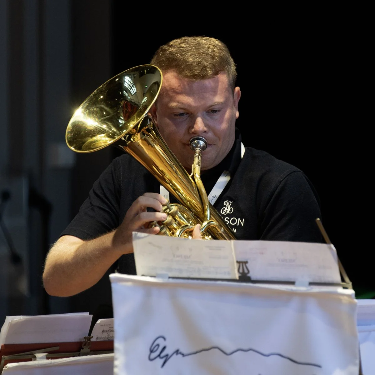 A man playing a brass instrument, possibly a euphonium, reading sheet music in a music stand.