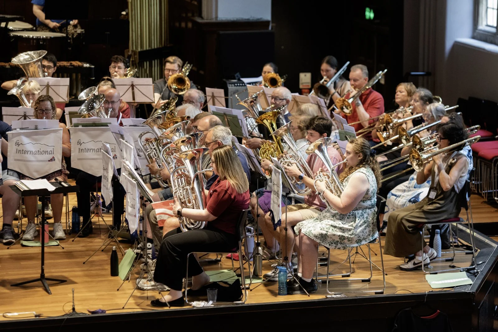 An orchestra of musicians playing brass instruments during a rehearsal or concert in a concert hall.