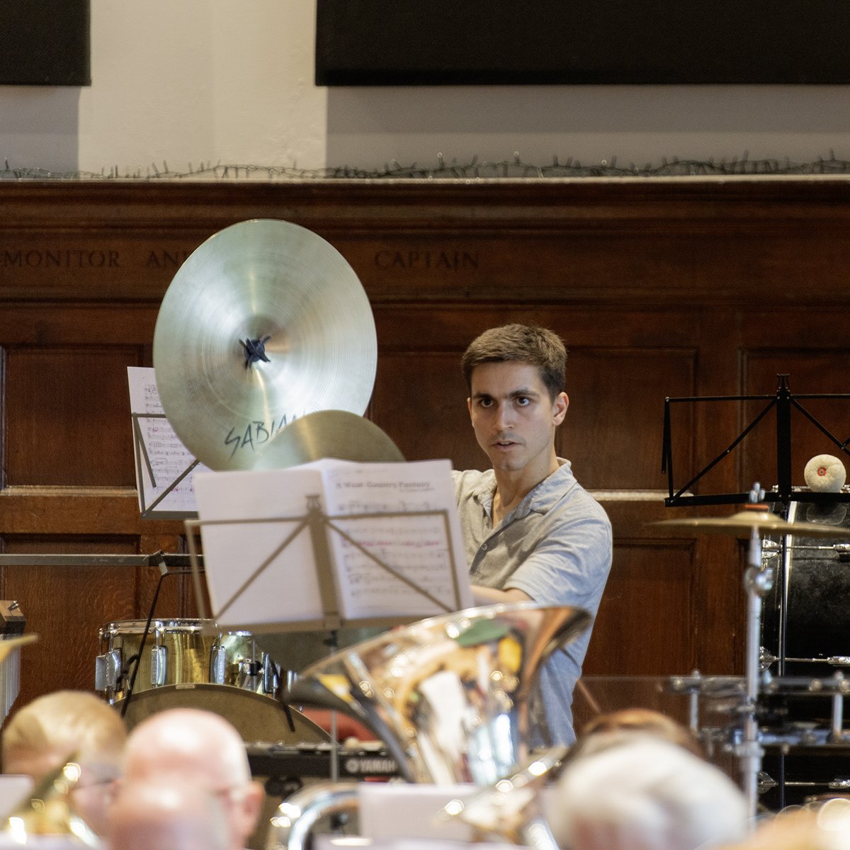 Young man playing percussion instrument in a musical performance with sheet music, cymbal, and other instruments around him.