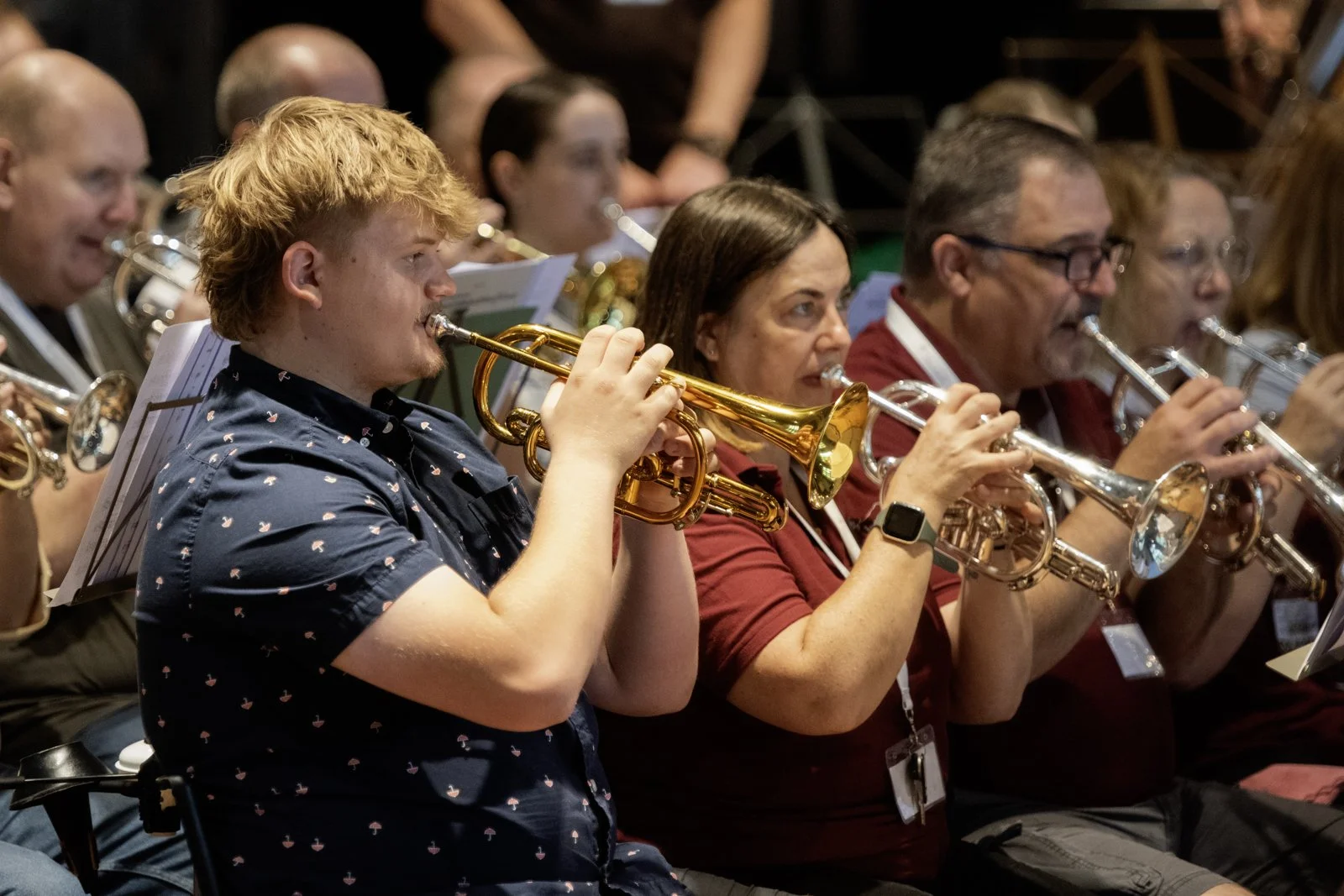 Group of people playing trumpets during a musical performance, seated indoors.