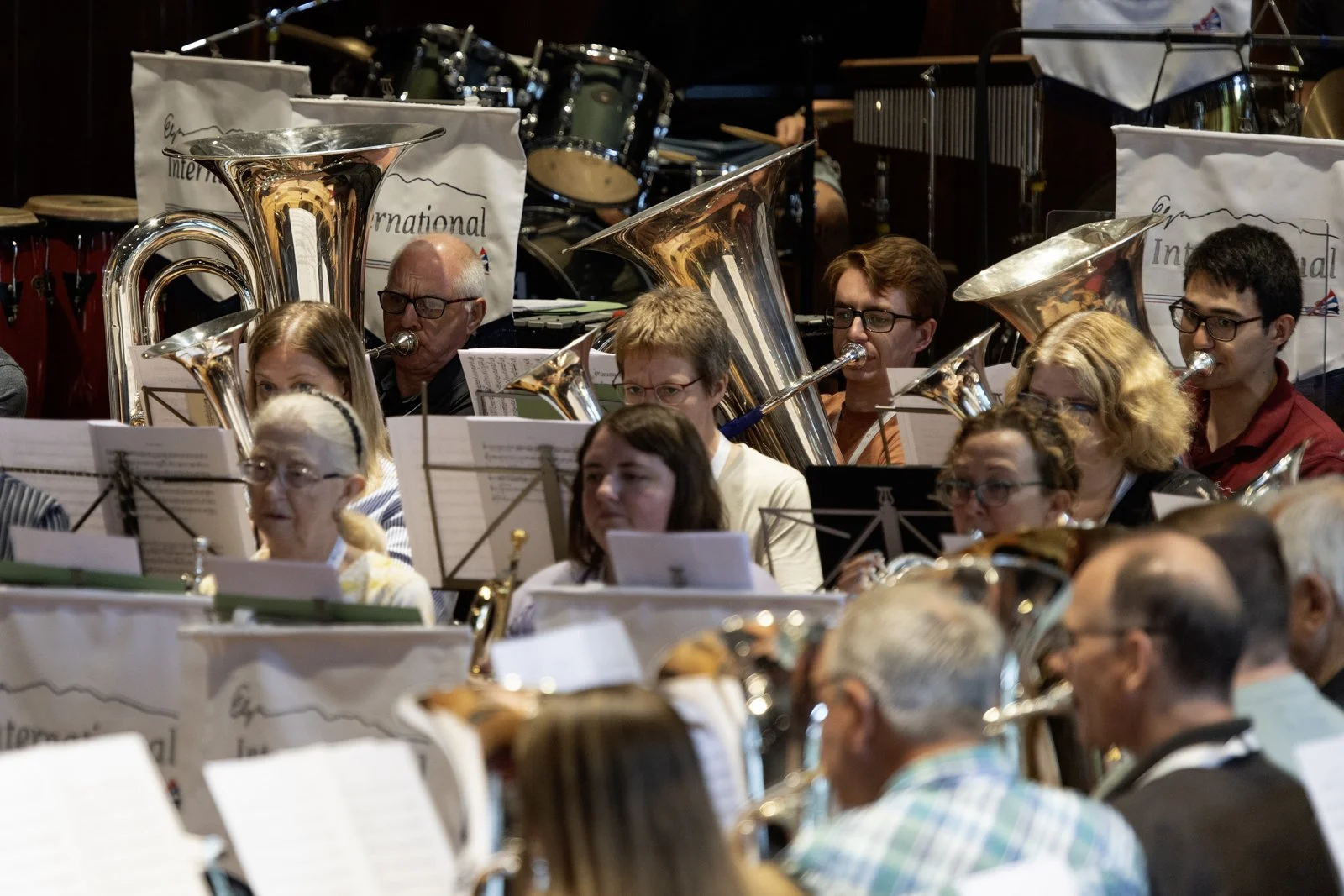 An orchestra performing, featuring musicians playing brass and percussion instruments, with sheet music in front of them.