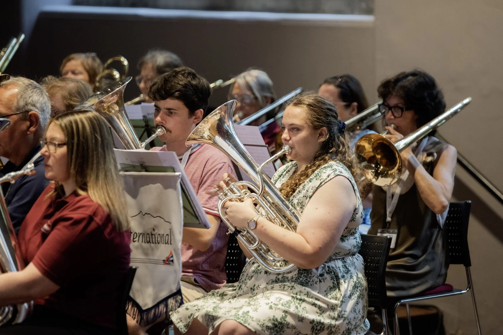 A group of musicians playing brass instruments during a concert, seated in a row, focused on their sheet music.