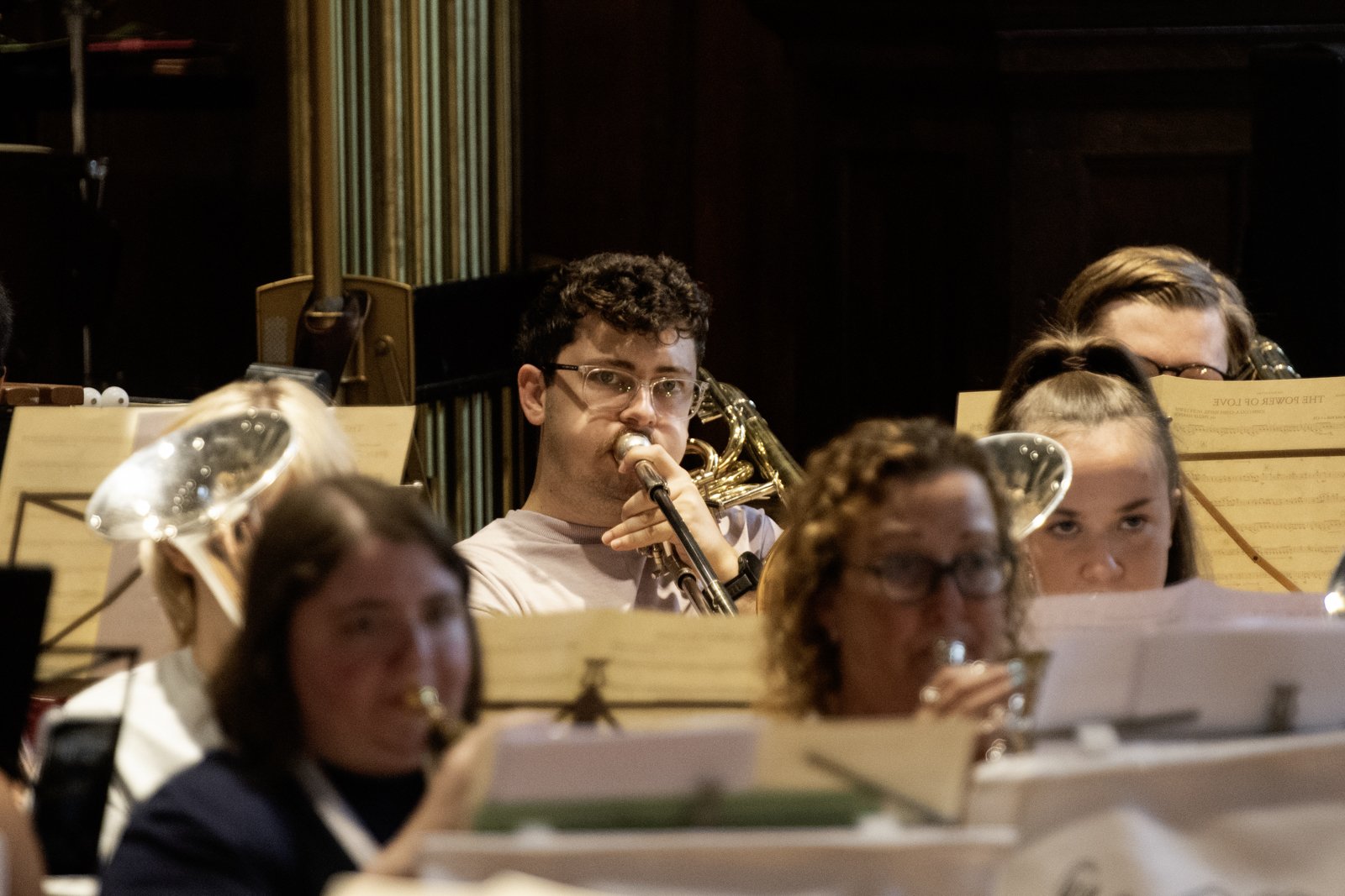 Group of musicians playing in an orchestra, focusing on a young man with glasses playing a clarinet in the center.