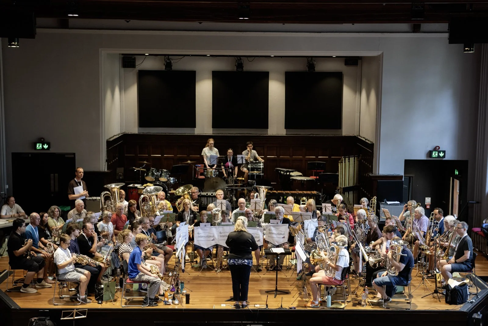 An orchestra rehearsing on stage in a concert hall with various musical instruments and a conductor leading them.