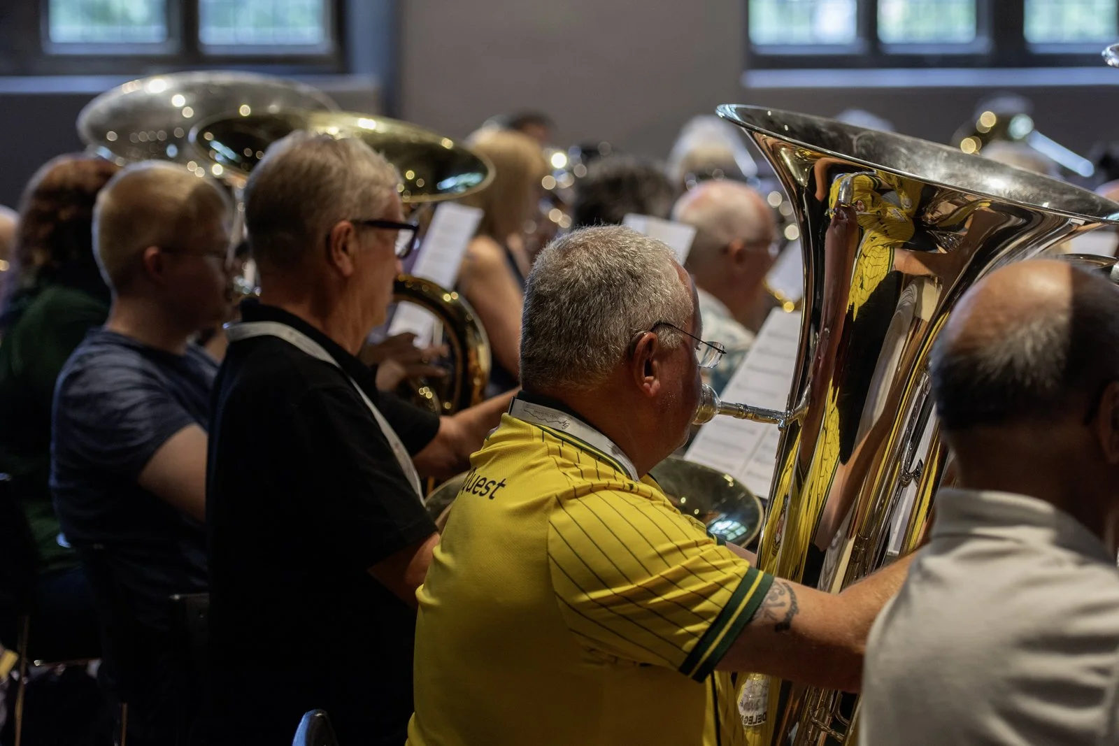 A group of people playing brass instruments in an orchestra indoors during a rehearsal or performance.
