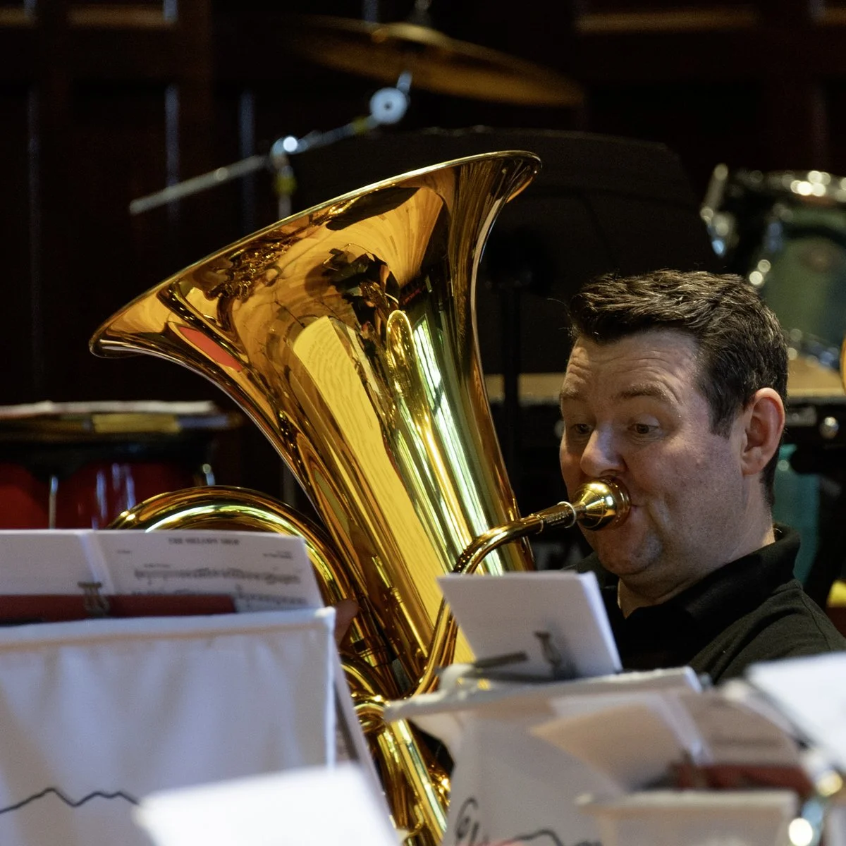 A man playing a shiny, gold-colored tuba, looking focused as he reads sheet music.