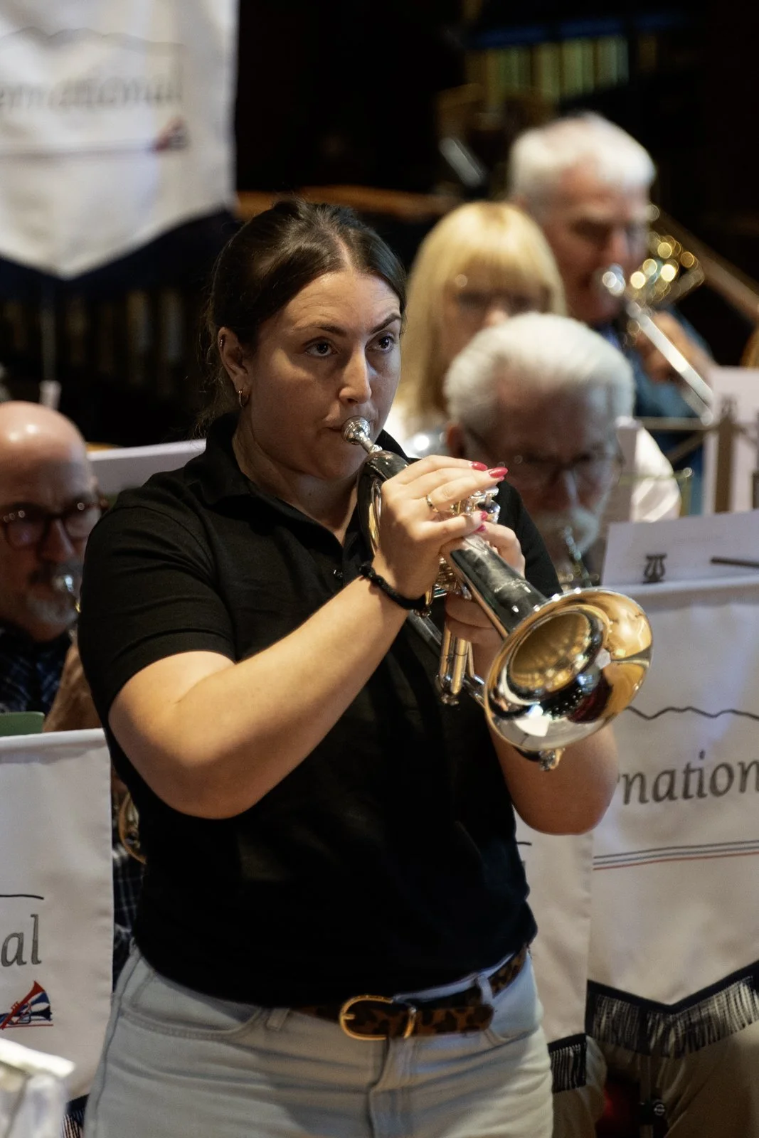 A woman playing a trumpet in a group setting, with other musicians behind her, in an indoor environment.