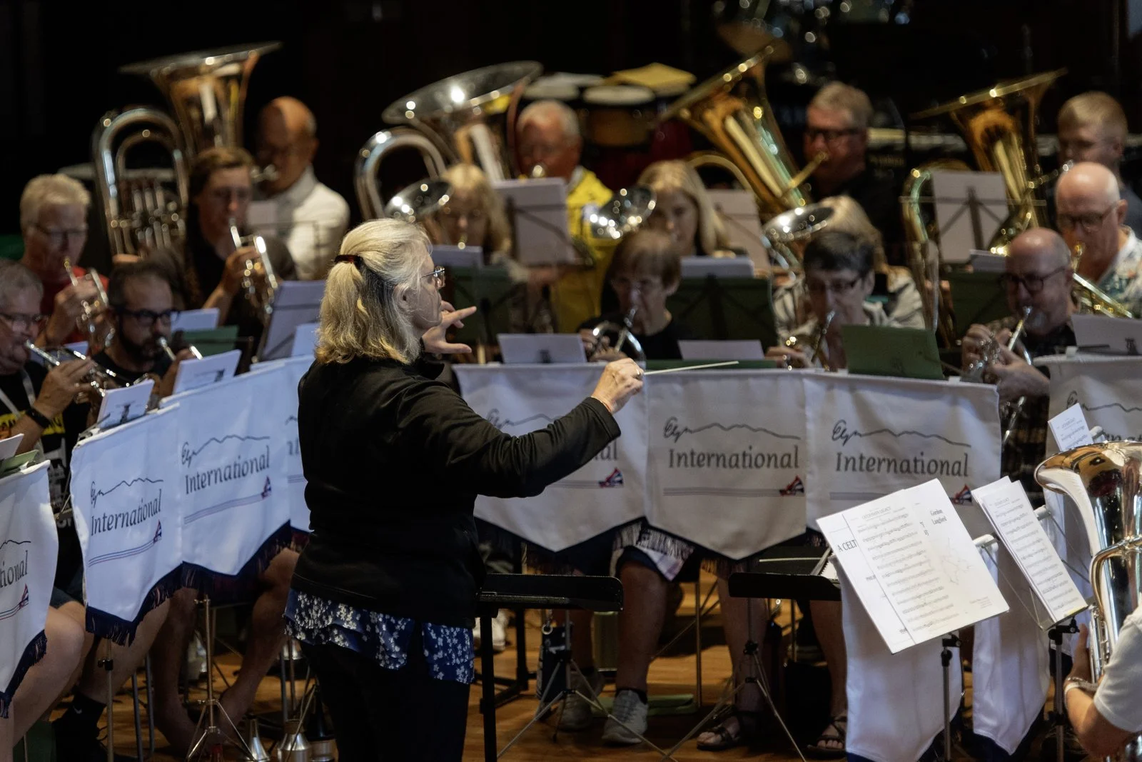 An orchestra performing on stage with a female conductor leading them, with banners that read 'International' in the front.