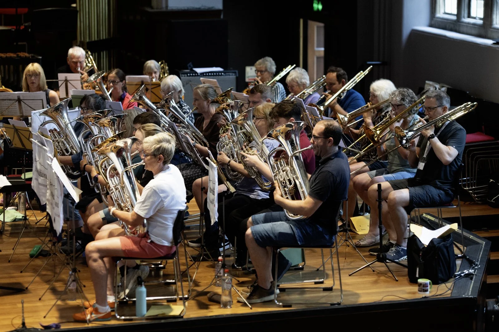 An orchestra rehearsal with musicians playing brass instruments in a large indoor space.