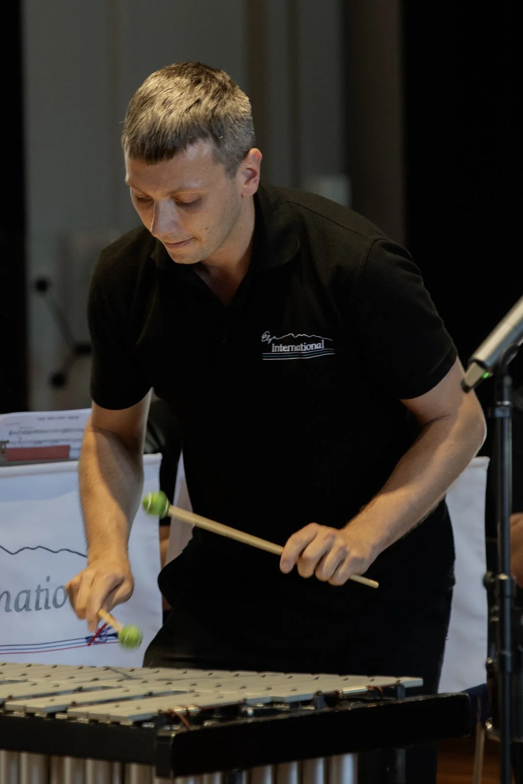 A man playing a mallet instrument at a performance or event, wearing a black shirt with a logo.