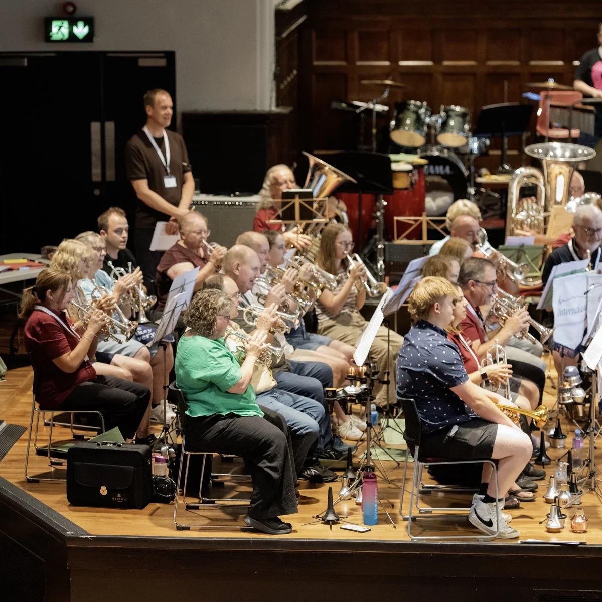 An orchestra performing on a stage with various musicians playing brass and percussion instruments, with music stands and water bottles nearby.
