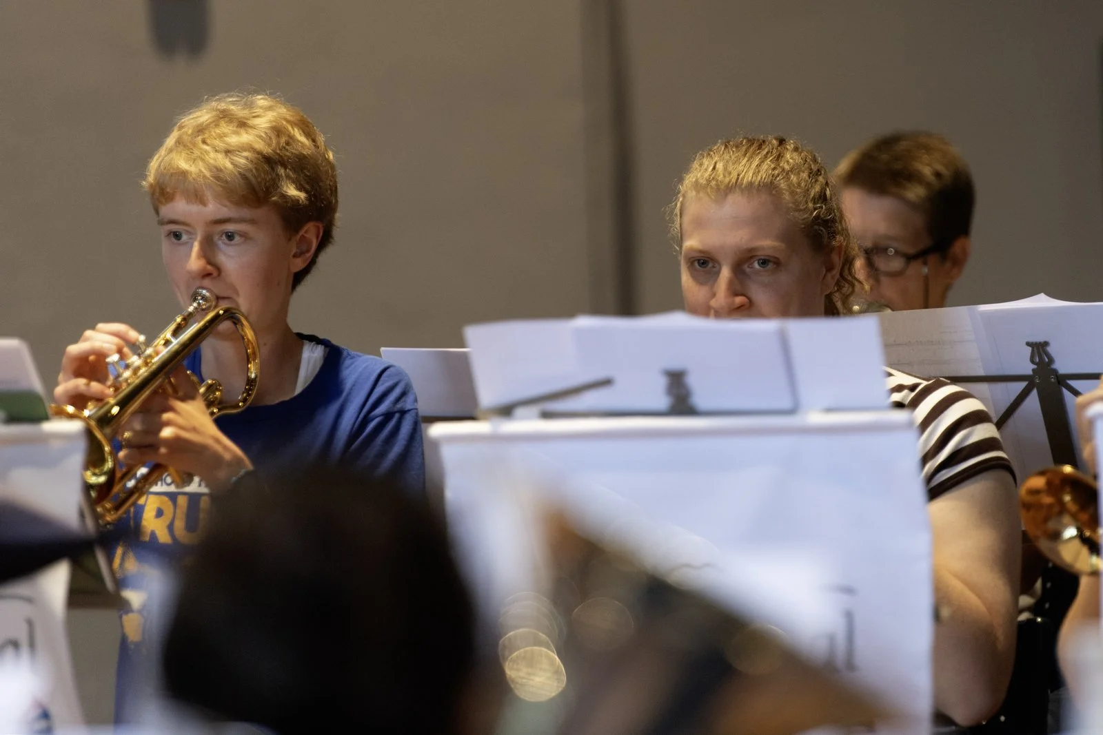 Young musicians in an orchestra, with one playing a trumpet and others reading sheet music.