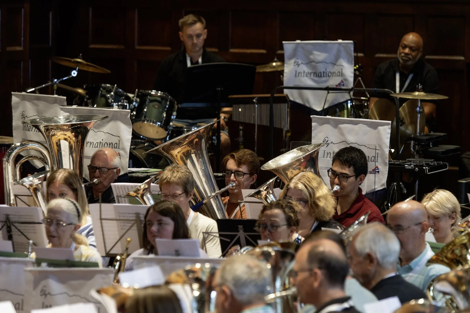 An orchestra performing, with musicians playing brass instruments and percussion in a concert hall.