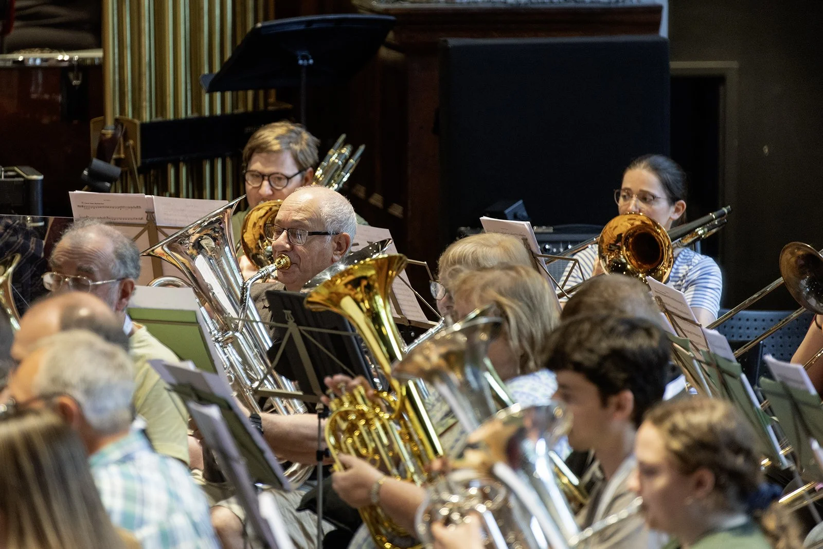 An orchestra performing with musicians playing various brass instruments, including saxophones and French horns in a concert hall.