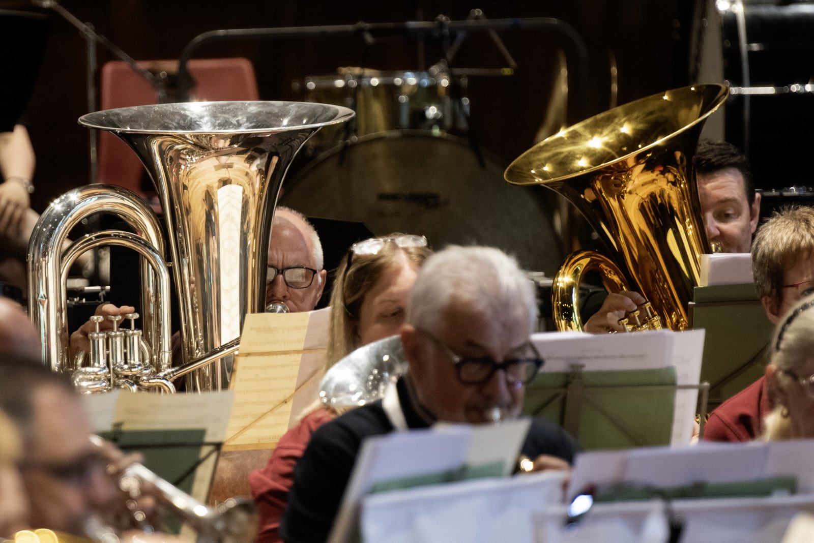 Orchestra playing, featuring large brass instruments like tubas, with musicians reading sheet music.