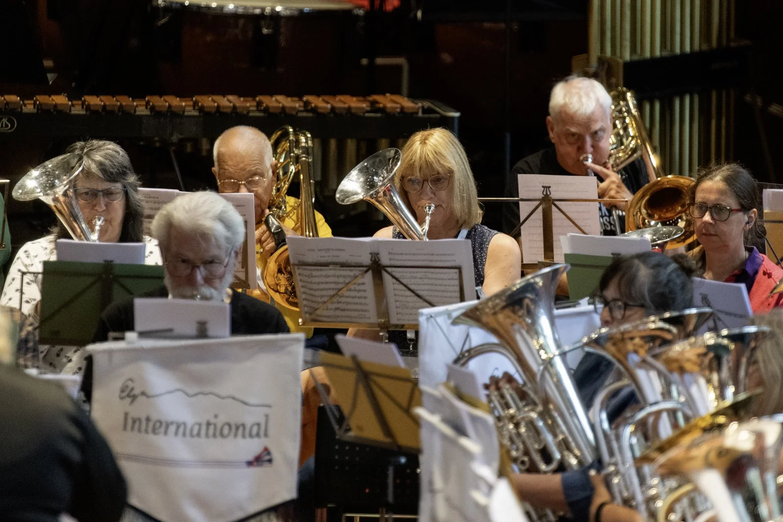 Group of musicians in an orchestra, playing brass instruments, reading sheet music during a performance.