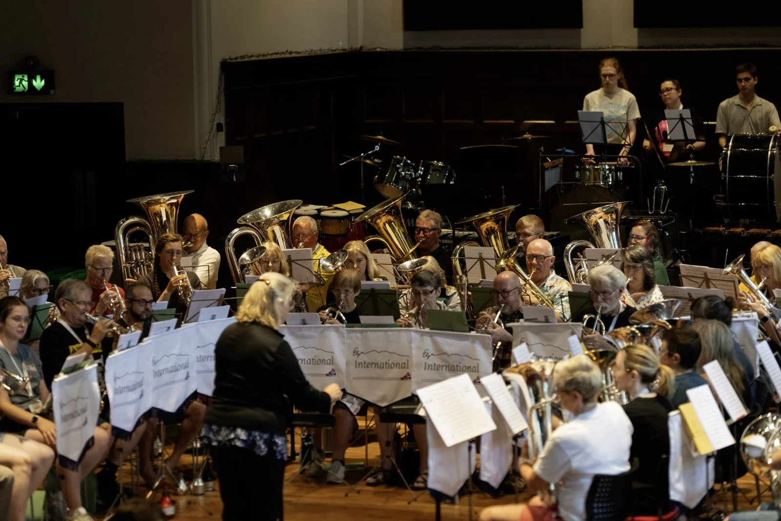 An orchestra performing in a concert hall with many musicians playing wind instruments and a conductor leading them.