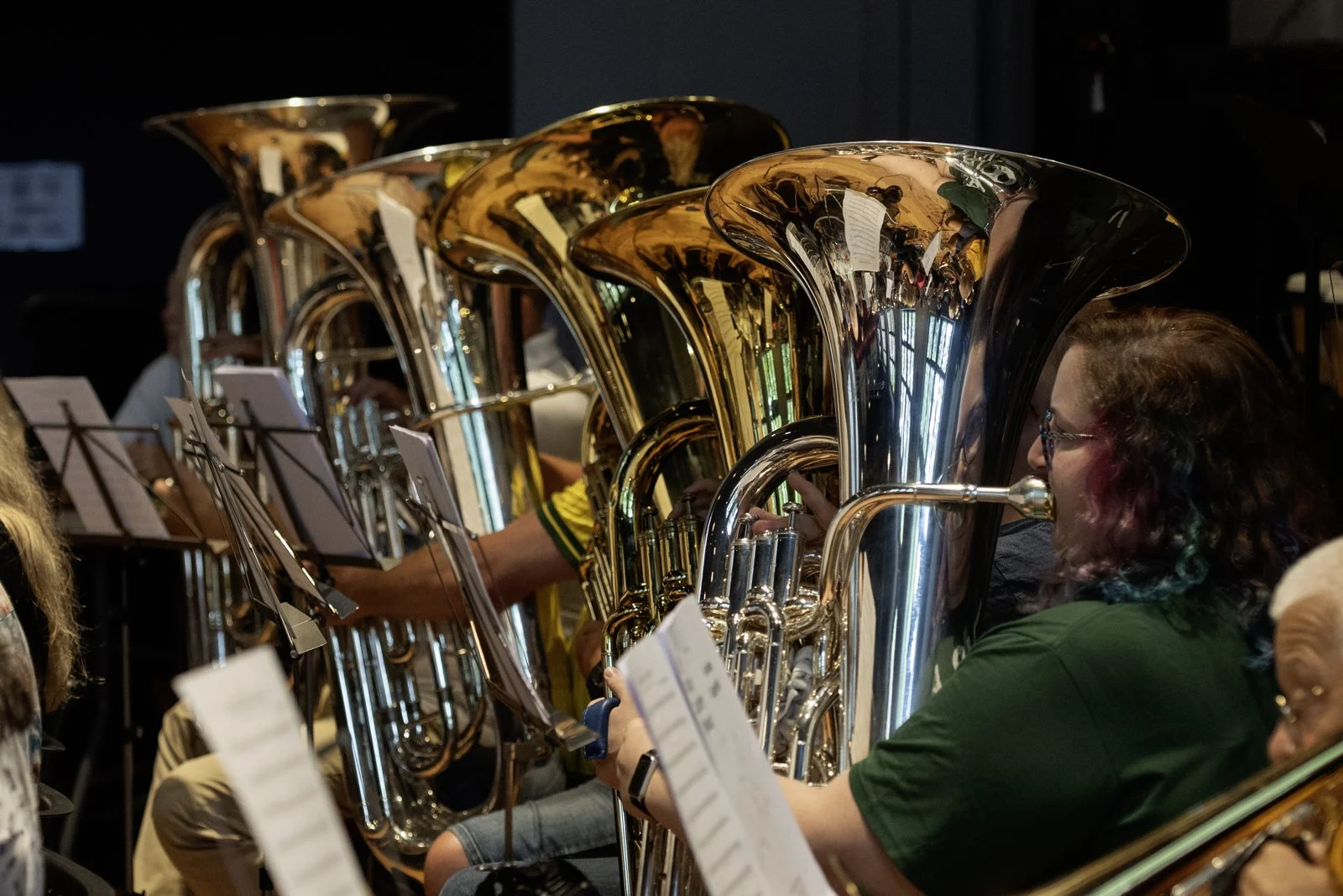 Group of musicians playing brass instruments, including tubas, during a concert or rehearsal.