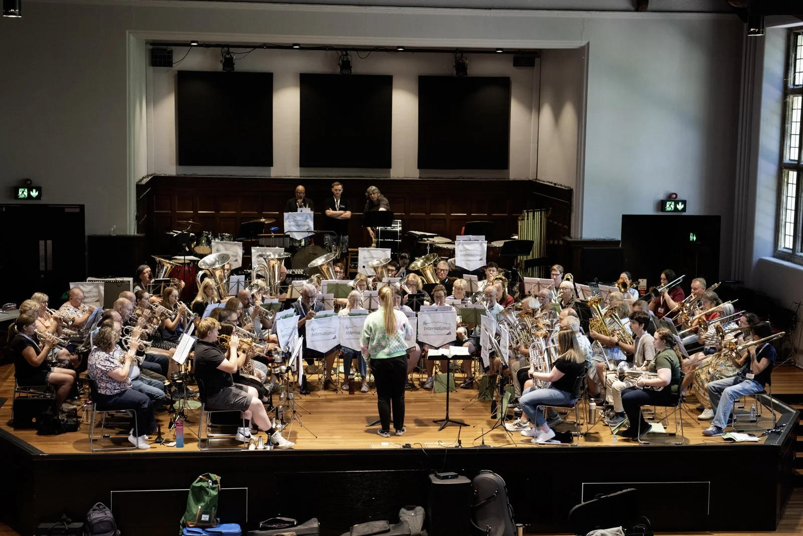Full view of a large orchestra performing on stage in a concert hall, with a conductor standing in front.