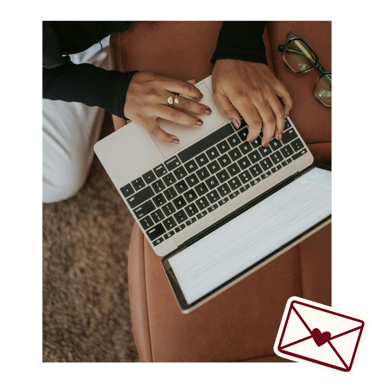 Person using a laptop with an open book on their lap, glasses on the side, sitting on a brown couch, and an envelope icon with a heart on it in the bottom right corner.