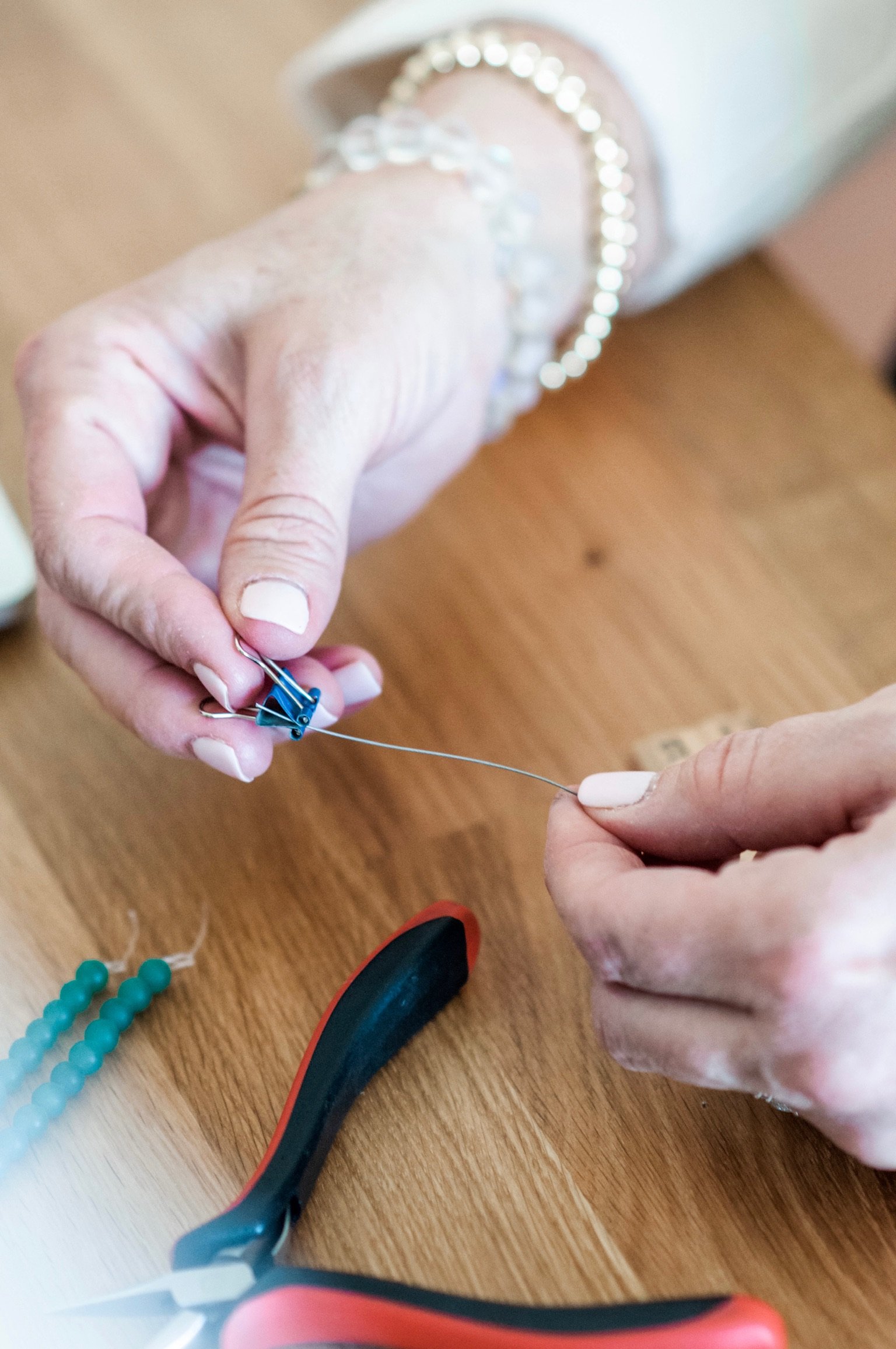 Close-up of hands attaching a small loop to a string with a pin, on a wooden table with sewing supplies nearby.