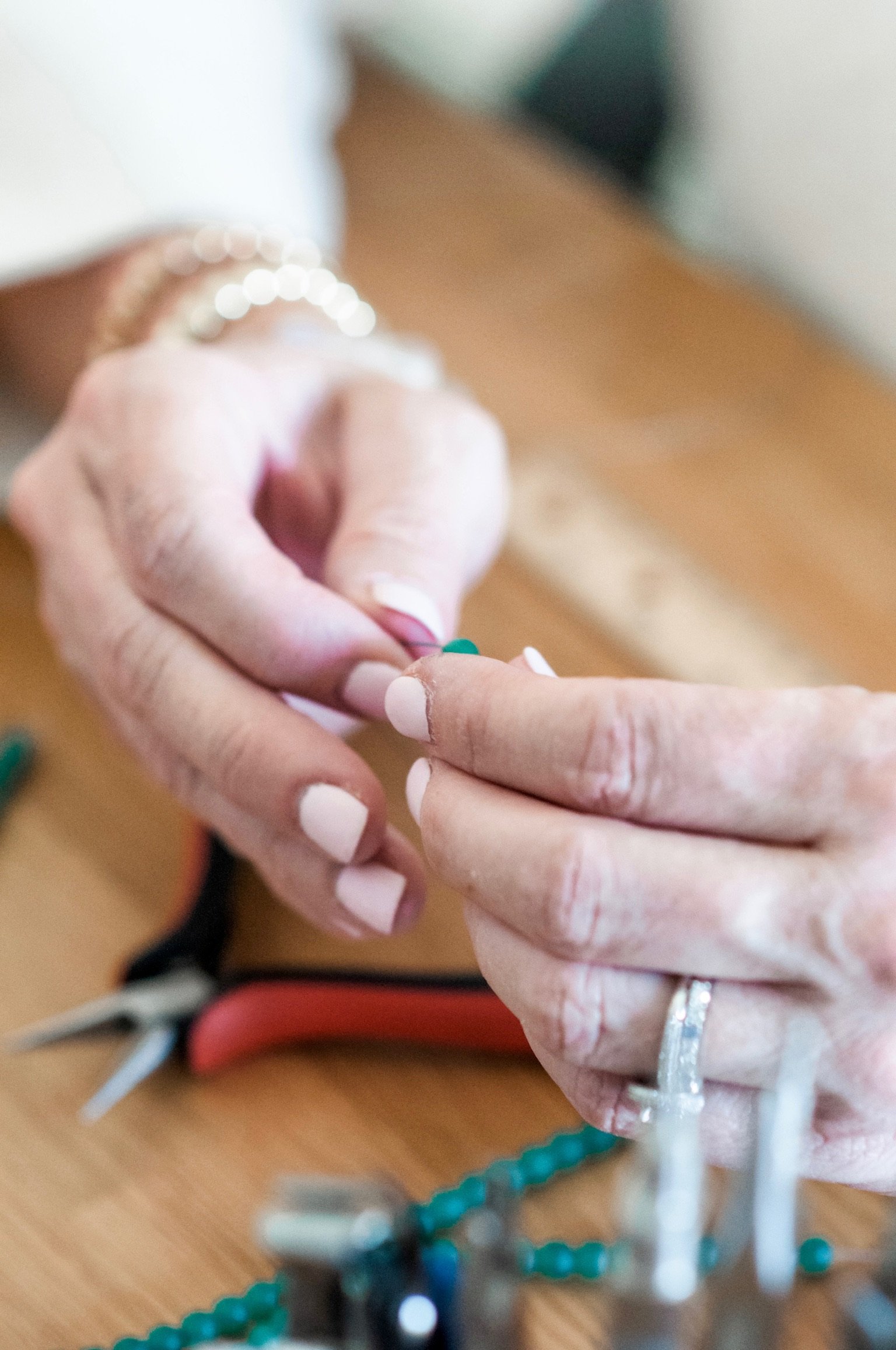 Close-up of a person's hand with an IV line inserted, with jewelry on the fingers. The background shows beaded jewelry and a pair of scissors on a wooden surface.