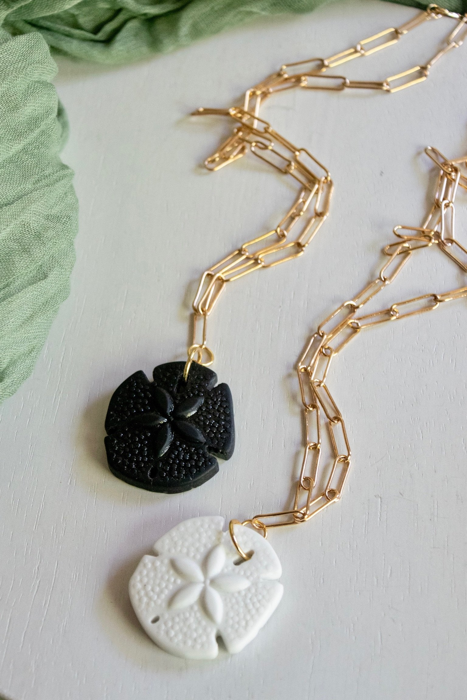 Close-up of a gold chain necklace with white and black carved flower pendant, green fabric in background.