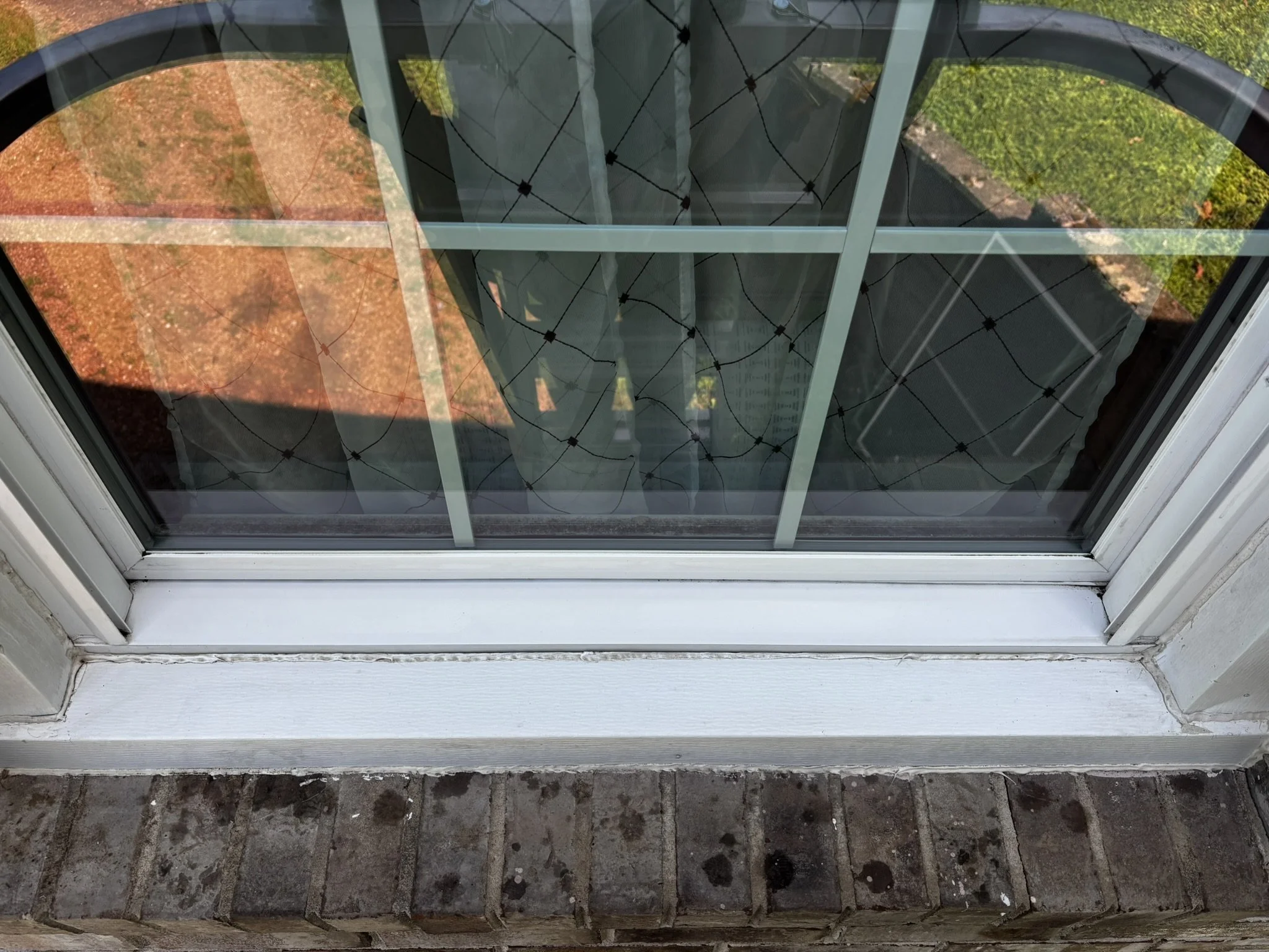 View through a glass door showing a brick patio area outside with some greenery, and the inside floor made of dark stone tiles.