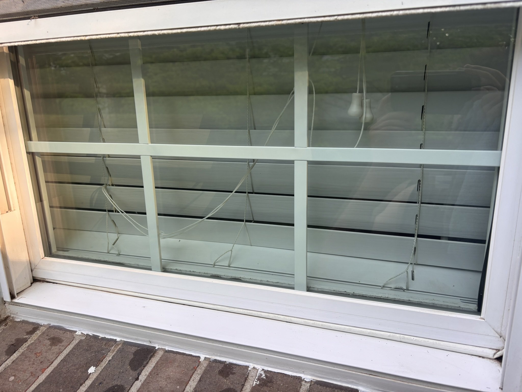 An empty storefront window with a metal security grill that is rolled up, revealing an interior with white walls and some wiring hanging, situated above a brick sidewalk.