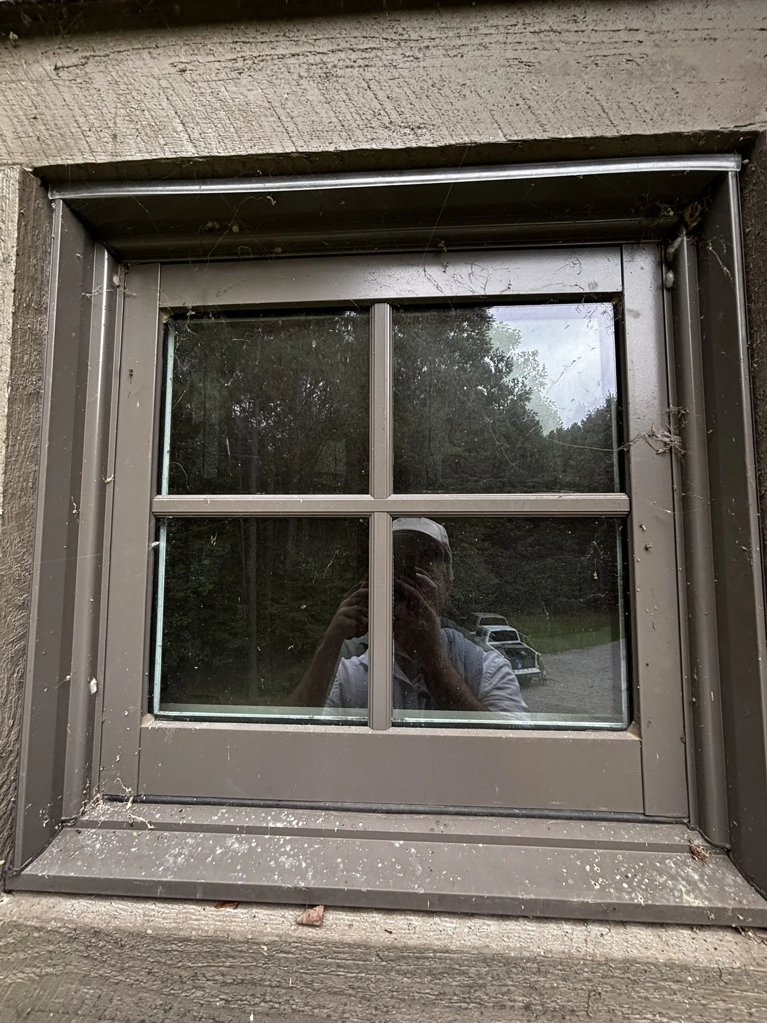 Close-up of a window with dirty glass and spider webs, set in a wooden exterior wall
