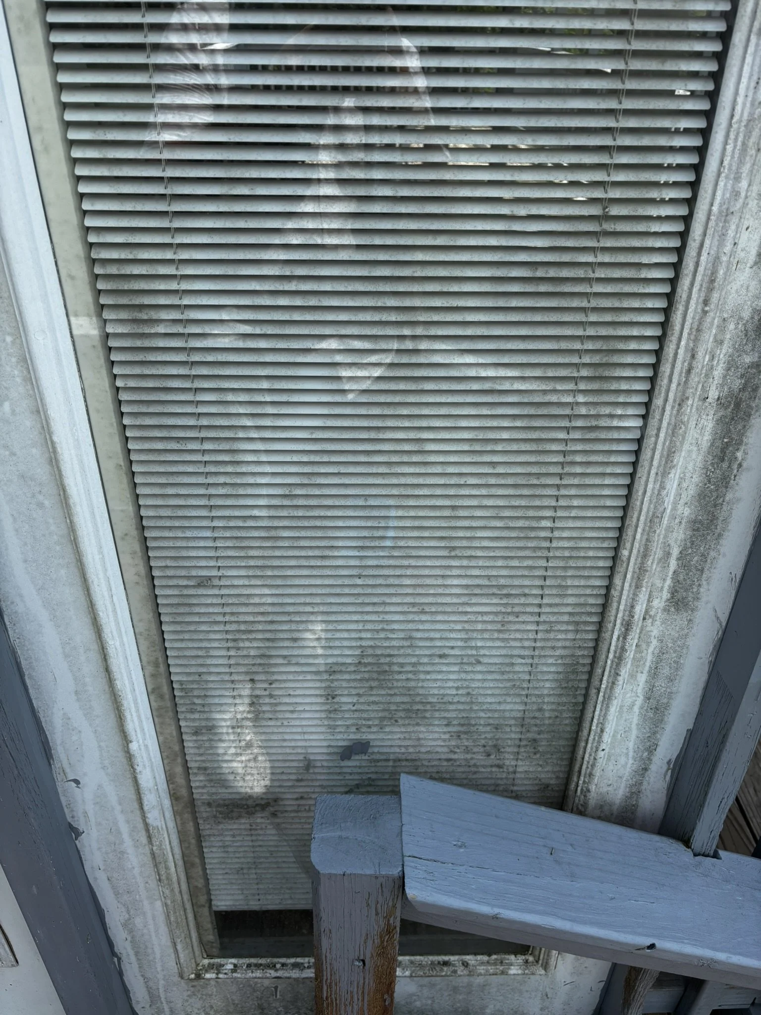 A dirty air vent on a weathered building exterior with a piece of wood blocking part of the lower section.