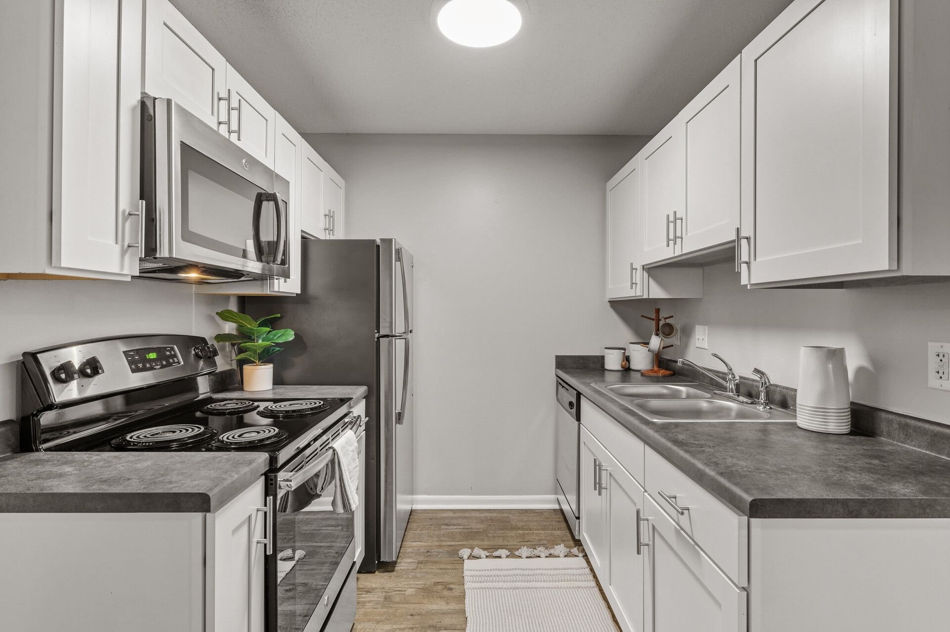 A modern kitchen with white cabinets, a stainless steel microwave and refrigerator, black stove, double sink, and small decorative items on the countertop found at Eastgate Apartments in White Bear Lake, MN
