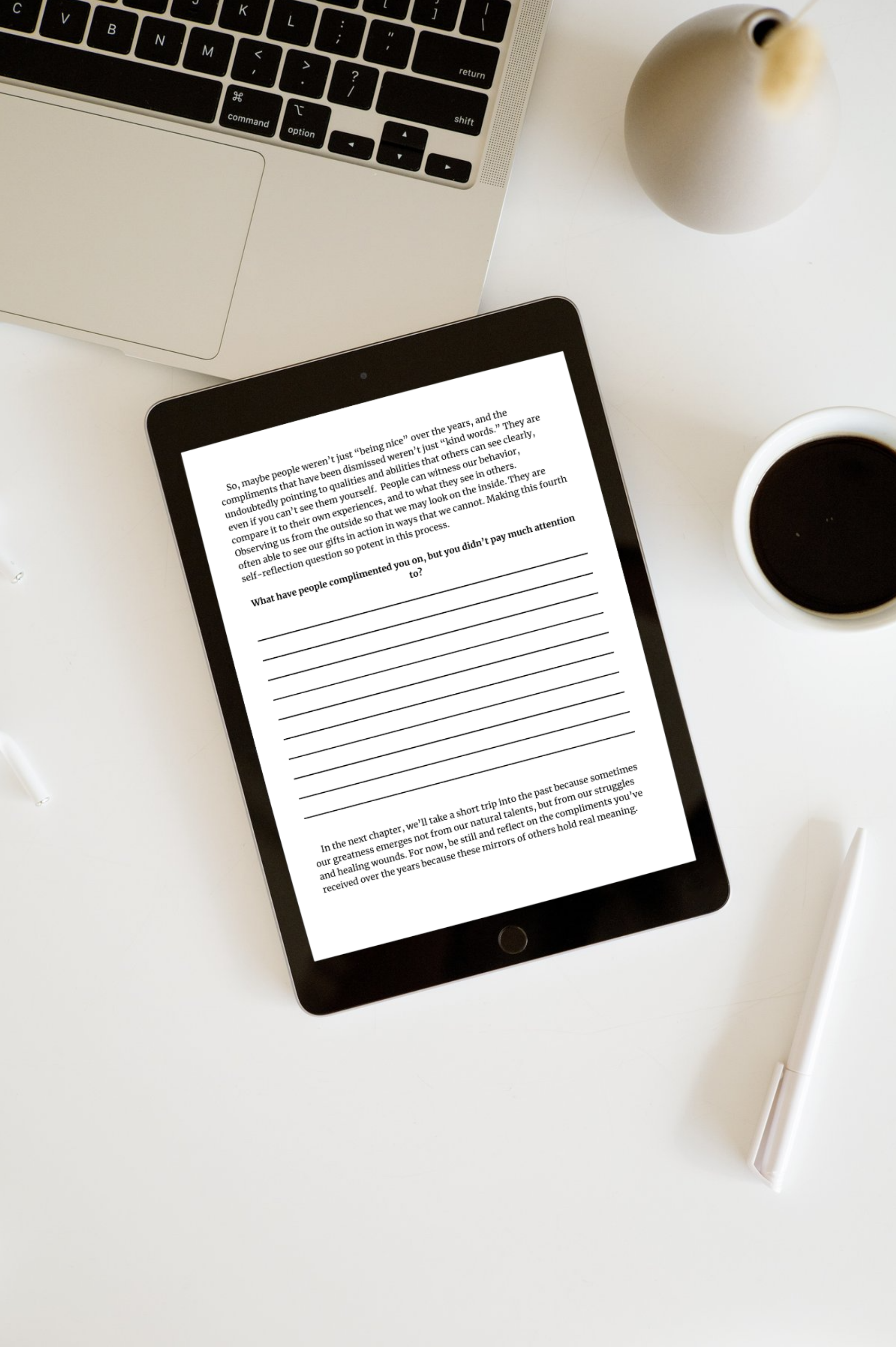 A flat lay of a workspace featuring a MacBook laptop, a tablet with text on its screen, a white pen, a cup of black coffee, and a small beige decorative vase on a white surface.