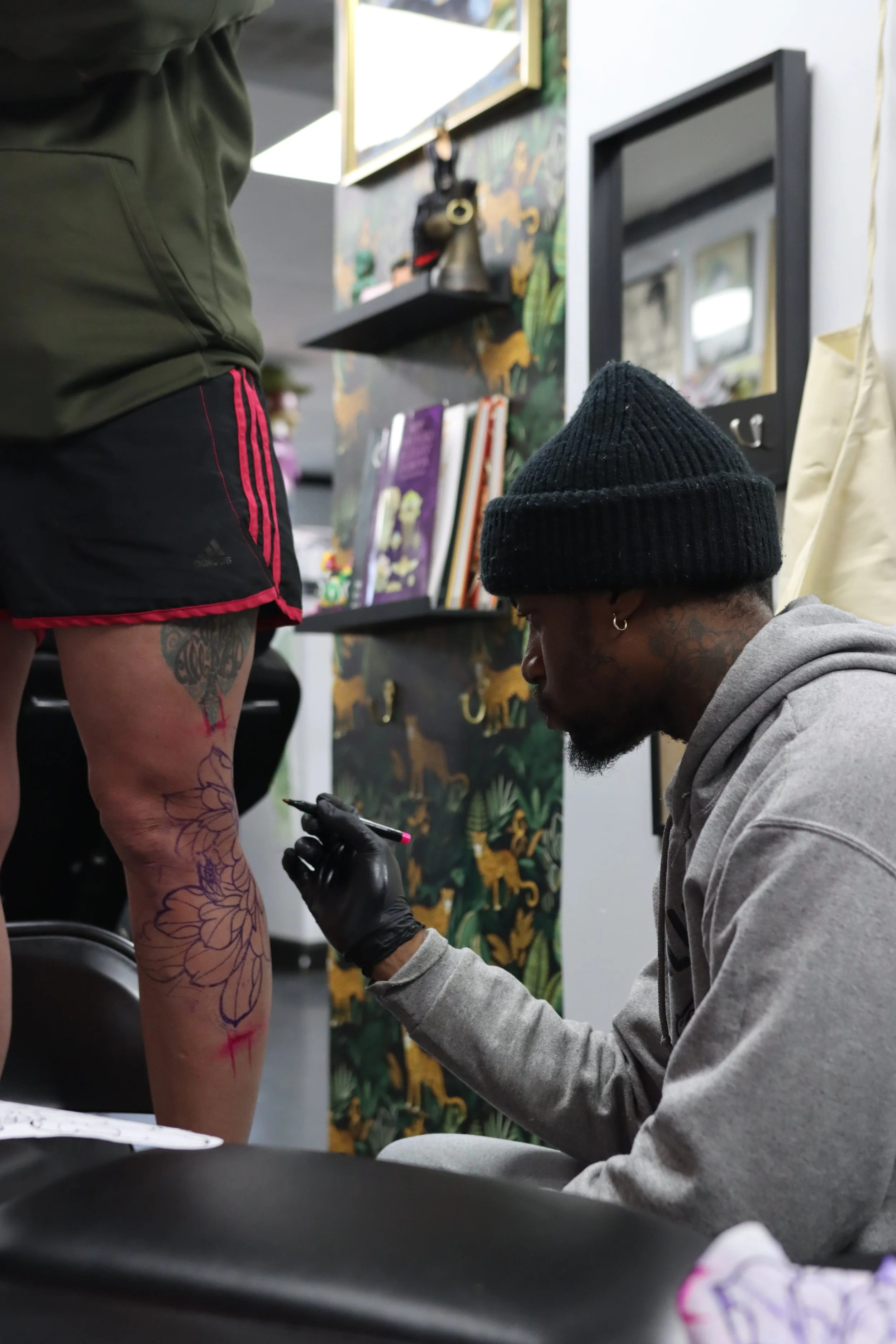 Tattoo artist working on a floral tattoo on a person's leg in a tattoo studio.
