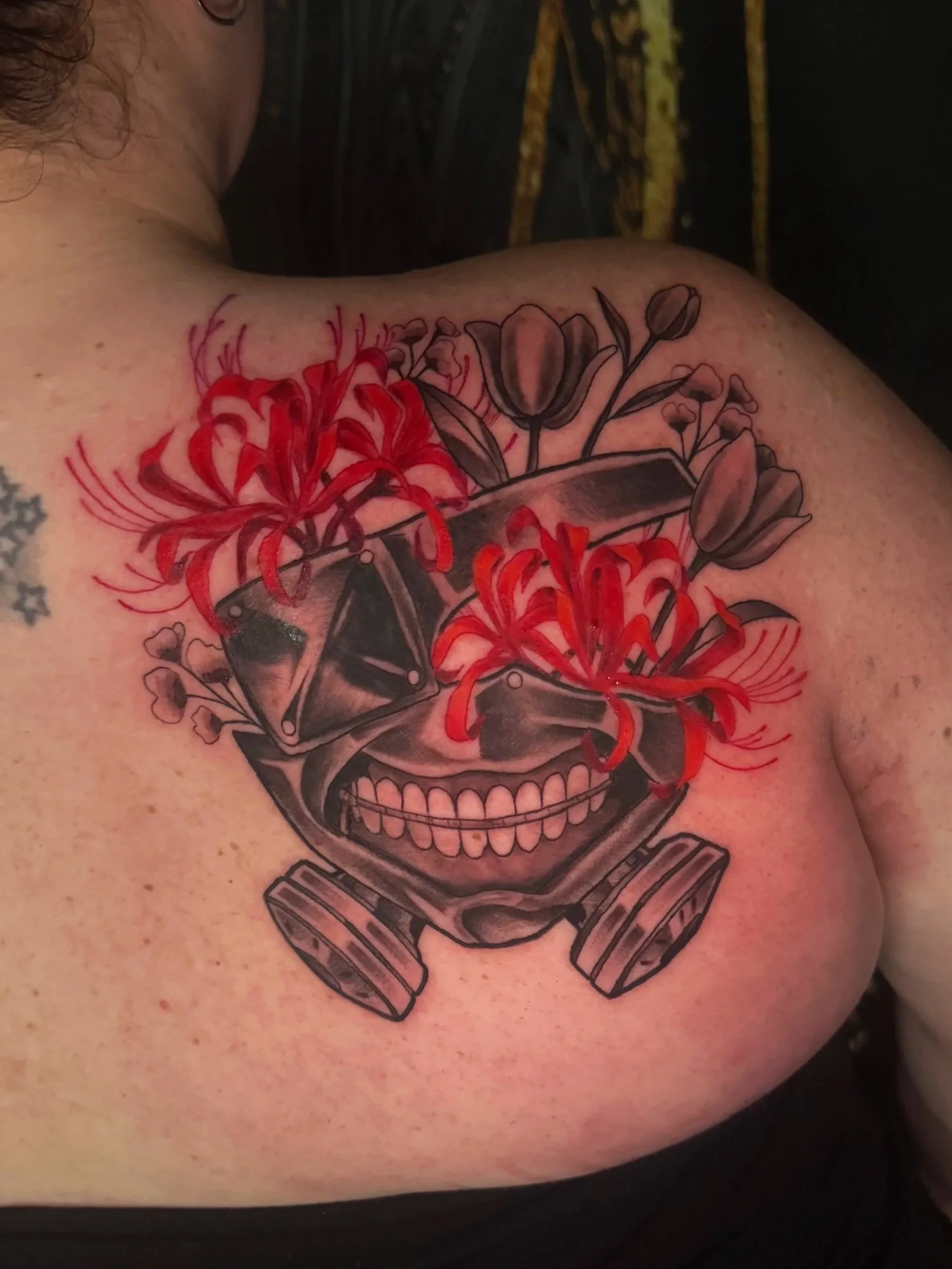 Tattoo of a skull with flowers and a knife on a person's shoulder.