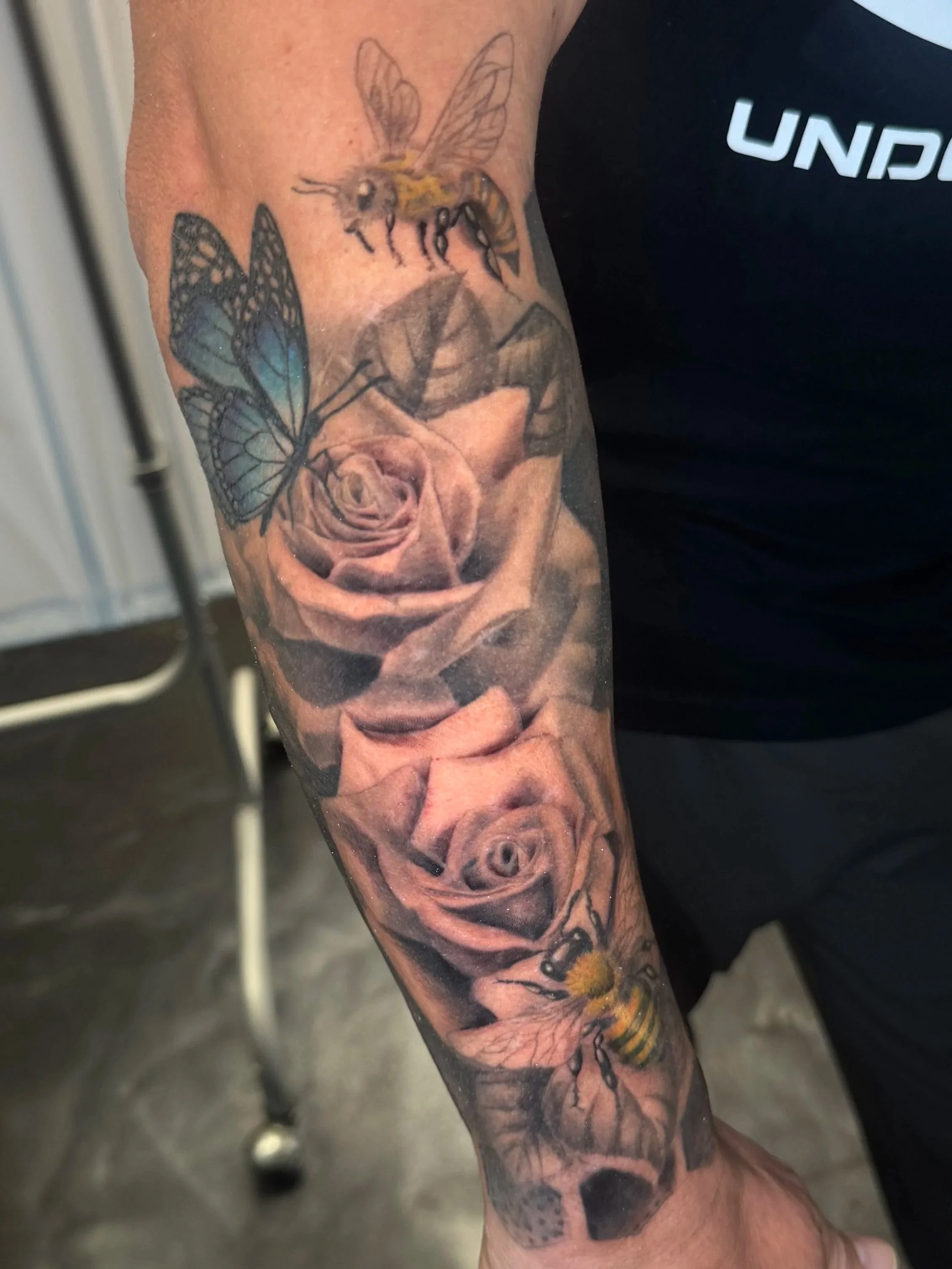 Tattoo of a bee, butterfly, and roses on a person's arm.